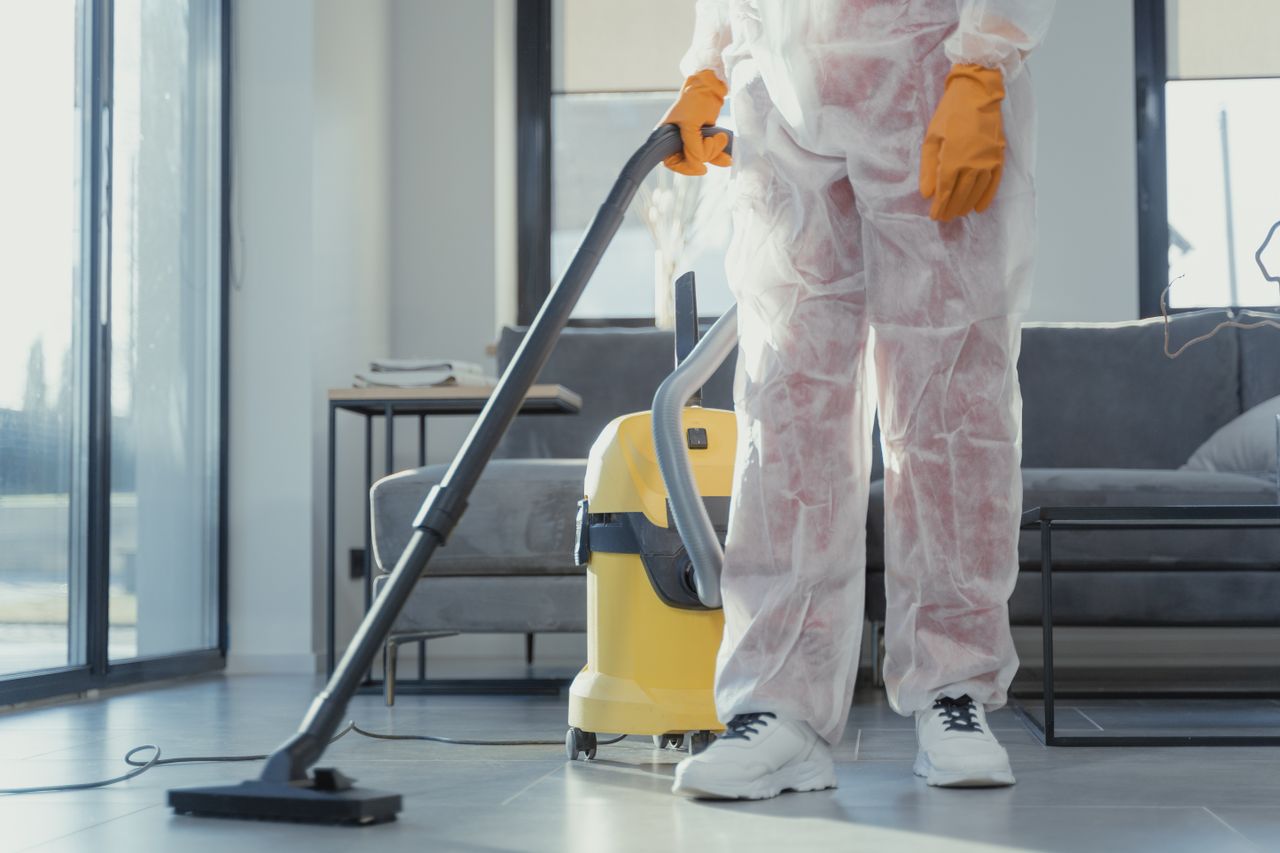 services-04 A cleaner in protective coveralls and gloves vacuuming a modern living room.