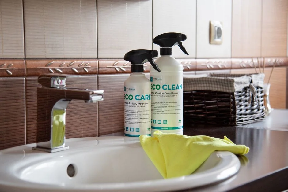 Hands in yellow gloves cleaning wall with sponge and spray bottle.